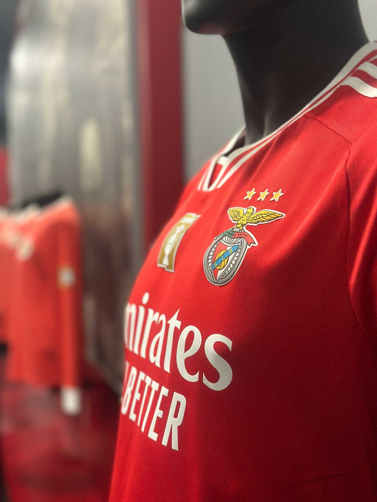 Camiseta oficial Sport Lisboa e Benfica, temporada 2023-24. Emirates Sponsor. En el fondo, camisetas clásicas de color rojo del SLBenfica. 