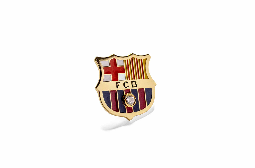 La insignia del FC Barcelona vista desde cerca, sobre fondo blanco. Con un diamante de 0.10 quilates engastado en su centro. 