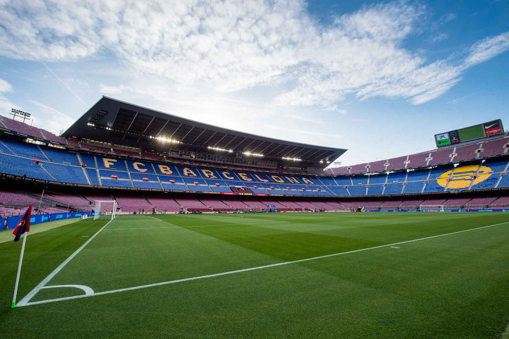 Vista panorámica del campo del Spotify Camp Nou desde un córner, con énfasis en el banderín del córner, el exuberante césped y la grada frente al icónico techo del estadio